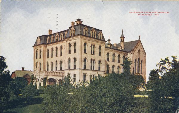 View across lawn with shrubs and trees toward the front entrance. A small red building is behind the hospital on the left. Caption reads: "Milwaukee Passavant Hospital, Milwaukee."
