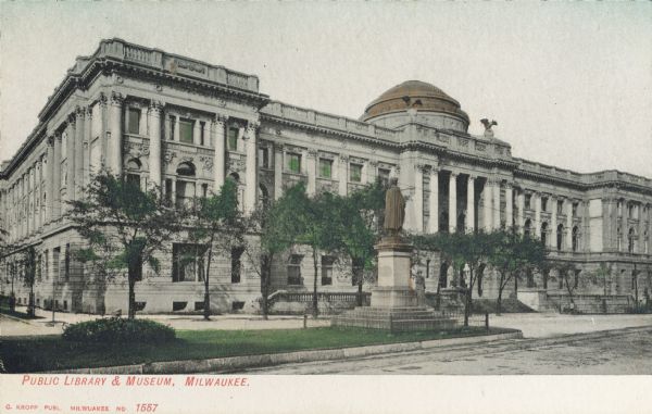 Front facade of building from across the street behind a median strip, which has a statue surrounded by a small fence. Caption reads: "Public Library & Museum, Milwaukee."