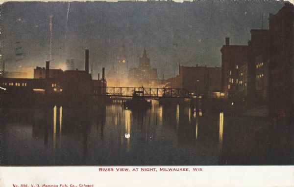 Railroad bridge over river and buildings at night. In the distance is a building with a clock tower. Caption reads: "River View, at Night, Milwaukee, Wis."