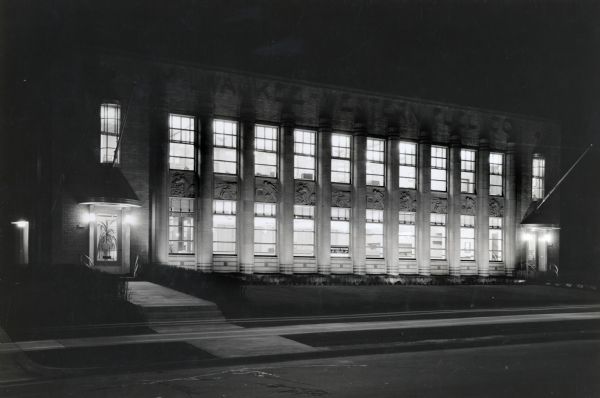 Nighttime view.  A small sign for the company is in a middle window on the first floor.  The left entrance has a potted plant in the window.