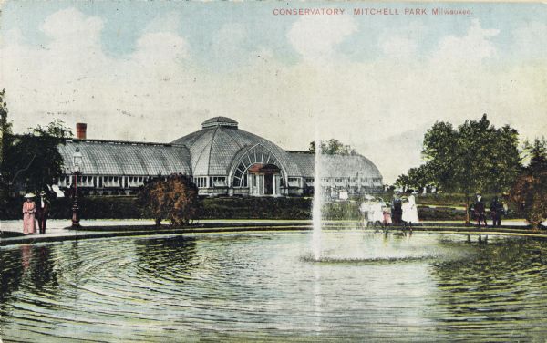 Fountain in front of the conservatory, separated by paths and shrubbery. Several pedestrians are standing near the fountain. Caption reads: "Conservatory, Mitchell Park, Milwaukee."