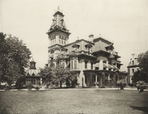 House at Ninth Street and Grand Avenue.  A large lawn is in the foreground.  The main building is centered with a tower on the left corner.  Separate buildings, including a greenhouse with a domed roof, are on either side of the house.