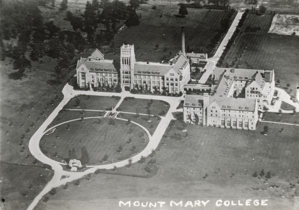 Aerial view of the college. Several buildings make up the college, surrounded by paths, roads, fields and trees. Caption reads: "Mount Mary College."