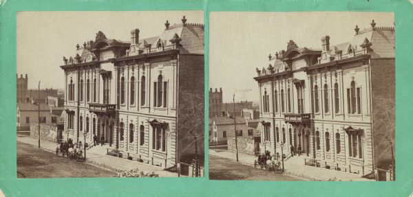 Stereograph; front of music hall along the road, with a horse and carriage team in front of the entrance.  Buildings can also be seen in the left background.