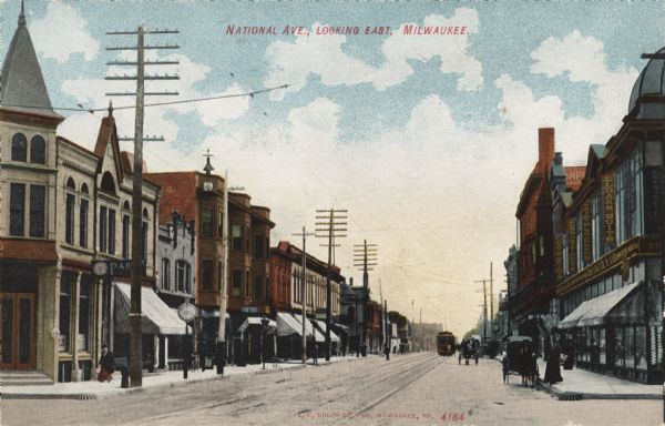View down National Avenue. Storefronts line both sides of the road, and there are horse-drawn vehicles, pedestrians, and a streetcar. Caption reads: "National Ave., Looking East, Milwaukee."
