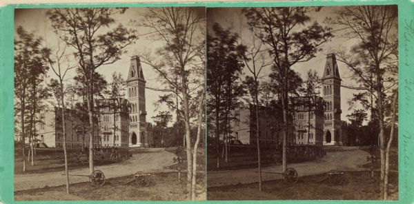 Stereograph. Looking northwest. Designed by Edward Townsend Mix, the building is said to be Wisconsin's premier example of the Victorian Gothic style of architecture.  Mix (1831-1890) was considered to be Milwaukee's leading architect after the Civil War.  The building is in the background, at the end of a curving drive.  Trees surround the grounds; a canon, a buggy, and a group of men are on the lawn along the drive to the entrance.