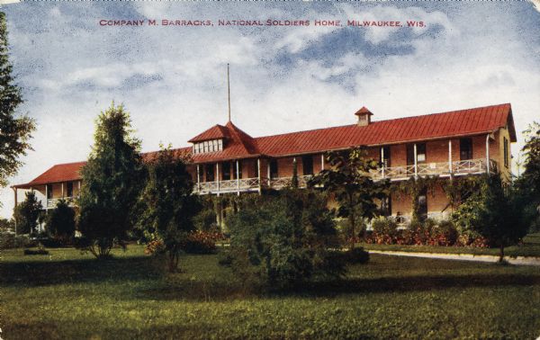 View across grounds toward the Company M Barracks, a two-story building with first and second floor porches. "Caption reads: "Company M Barracks, National Soldiers Home, Milwaukee, Wis."