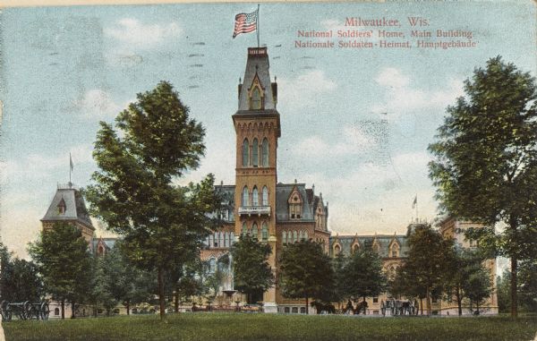 Front view of main building behind trees on the lawn.  A fountain is in front of the entrance. A flag is on the top of the building. Caption reads: "Milwaukee, Wis. National Soldiers' Home, Main Building. Nationale Soldaten Heimat * Hauptgebaude.
