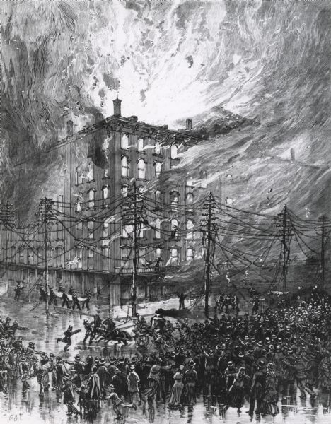 A large crowd is on the street surrounding the burning building.  Fire fighters are struggling with horses pulling the fire engine, and on the left a group of fire fighters have a sheet to catch falling people.  The power lines are broken and burning.
