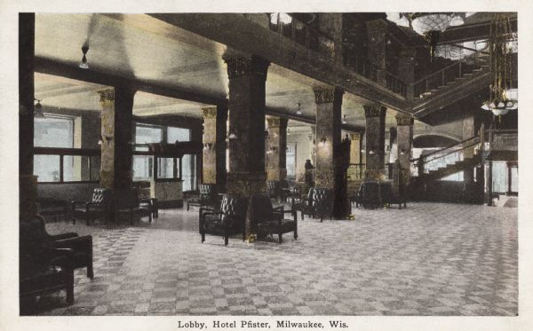 Interior view of lobby, with large chandeliers hanging from the ceiling, columns, stairway leading to second floor, and chairs positioned about the entrance. Caption reads: "Lobby, Hotel Pfister, Milwaukee, Wis."