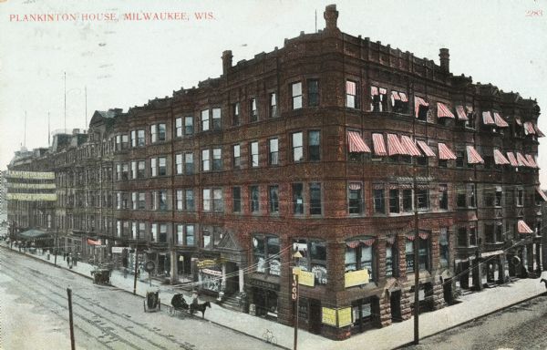 Elevated view looking east on Grand Avenue from the corner of Grand Avenue and 2nd Street. Plankinton Block was located between West Water (now Plankinton Street) and N. 2nd. It housed Plankinton House Hotel until 1915. The top two floors on the right have red and white stripped awnings over the windows. The bottom two floors have advertising signs in many of the windows. A horse and cart is sitting on the left. Caption reads: "Plankinton House, Milwaukee, Wis."