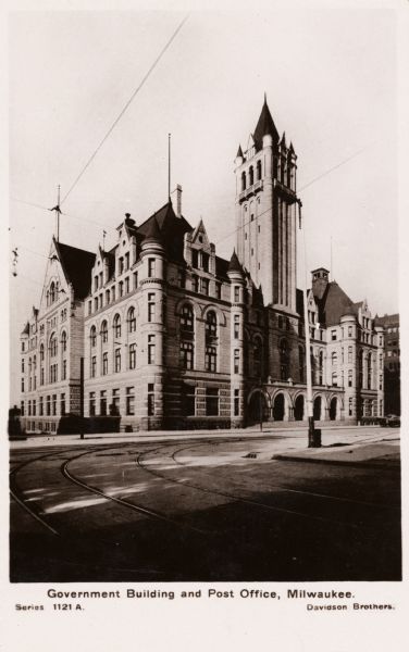 Tower of building is on the right. The road curves in front of the building, with trolley tracks visible.