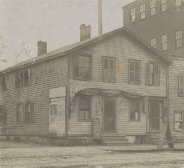 A pioneer Scandinavian immigrant hotel on Clinton Street, south side, built before the Civil War. Posters are a board on the left side of the house, and a hand-lettered signboard near the front door and a sandwich board on the sidewalk advertises hot coffee and pie.