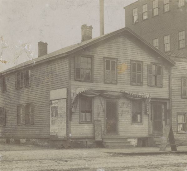 A pioneer Scandinavian immigrant hotel on Clinton Street, south side, built before the Civil War.  Posters are a board on the left side of the house, and a hand-lettered signboard near the front door and a sandwich board on the sidewalk advertises hot coffee and pie.