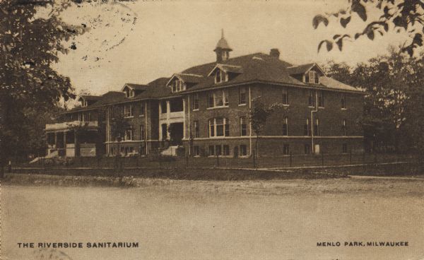 View across road toward the building which is surrounded by a fence. Caption reads: "The Riverside Sanitarium, Menlo Park, Milwaukee."