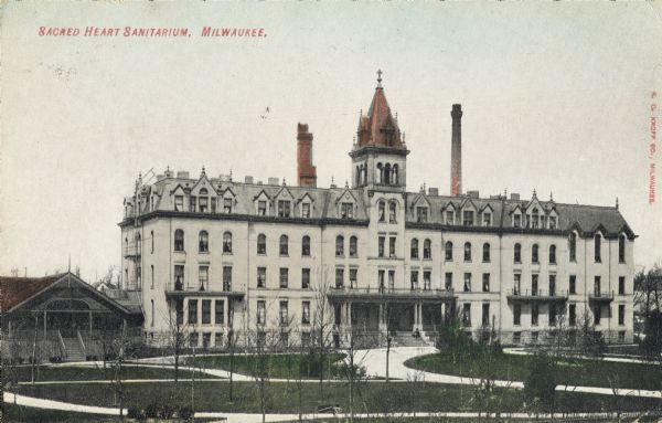 View across grounds toward the main building in the center with a lawn and paths in front. On the far left is a small attached building with a front porch. Caption reads: "Sacred Heart Sanitarium, Milwaukee."