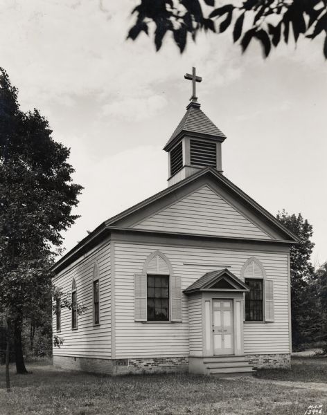 The first Catholic church in Milwaukee. The structure is shown here after it was moved to the grounds of St. Francis Seminary, St. Francis Wisconsin. It was subsequently relocated to Old World Wisconsin near Eagle. A small church with a basic cross on the steeple.  The foundation stone with the year 1839 is in the front lower left of the building.