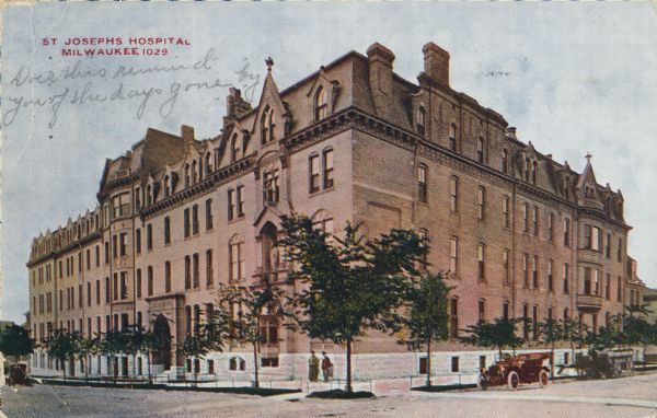 A motorcar and a horse-drawn carriage are parked on the right of the building. Caption reads: "St. Joseph's Hospital, Milwaukee."