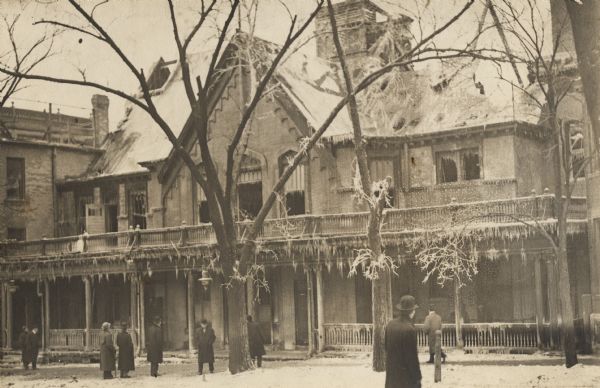 Formally a Universalist Church (under Rev. Augusta Chapin), then a Baptist church, later a club house and eventually a dance hall.  Photograph taken after a fire inside the building.  Several men are milling about the outside, looking at some of the damage.  Snow covers the area.