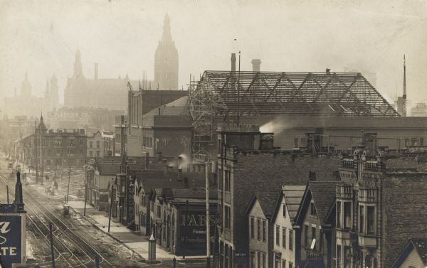 Elevated view looking east between Second and Third streets.  City Hall is visible in the left center background.  Signs and billboards dot several buildings. The skeleton of a roof being built and some scaffolding are on the right.