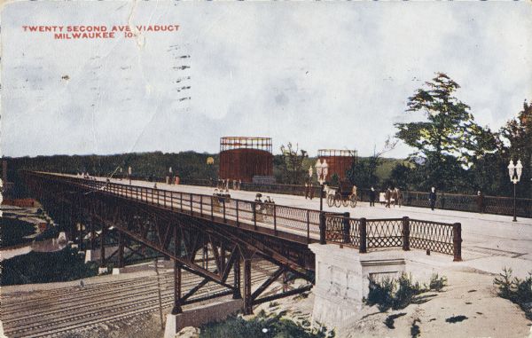 Looking north at the Menomonee Valley. Road incorrectly identified on the postcard as twenty-second street viaduct. Pedestrians and carriages are crossing the viaduct. Below are railroad tracks, and behind are large gas holders of the Milwaukee Gas Light Co. Caption reads: "Twenty Second Ave. Viaduct, Milwaukee."
