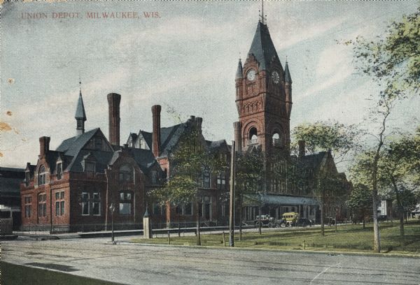 Union Depot with clock tower. Railroad station on left side, with clock tower. Park area on right with horse-drawn vehicles near the entrance. Caption reads: "Union Dept, Milwaukee, Wis."