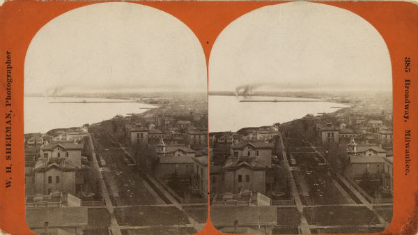 Stereograph. Elevated view looking roughly south, the foreground overlooks a residential neighborhood. On the far shoreline, smoke clouds spew out from large chimneys.