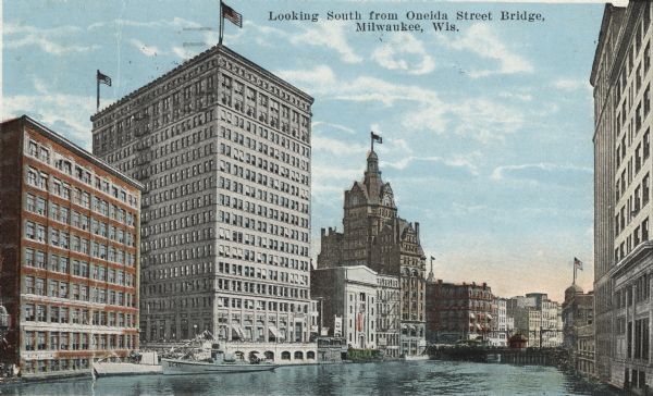 Looking south from Oneida Street Bridge. Large buildings line the river edge. Another bridge is in the distance. Several buildings have flags on the roofs, and a few boats are on the river. Caption reads: "Looking South from Oneida Street Bridge, Milwaukee, Wis."