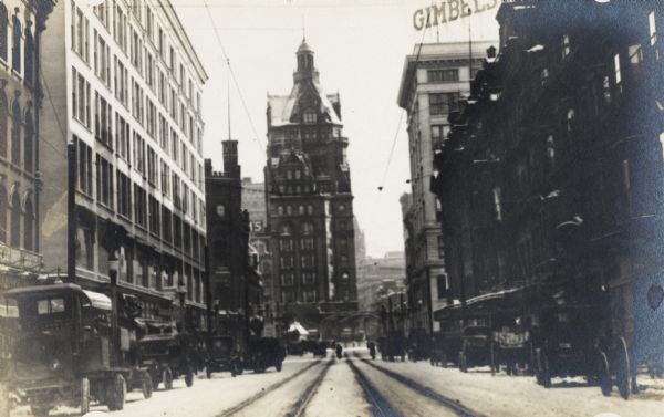 Looking down Grand Avenue to the east. The road is lined with automobiles, and cable car tracks are on the snow-covered street. A sign for Gimbel's is on top of a building on the right.