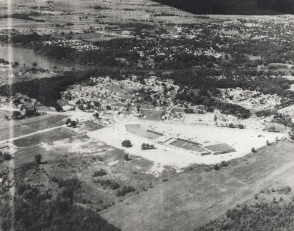 Aerial view of Valley Fair Mall, with a residential area beyond it on both sides of a river, all surrounded by trees and farmland.