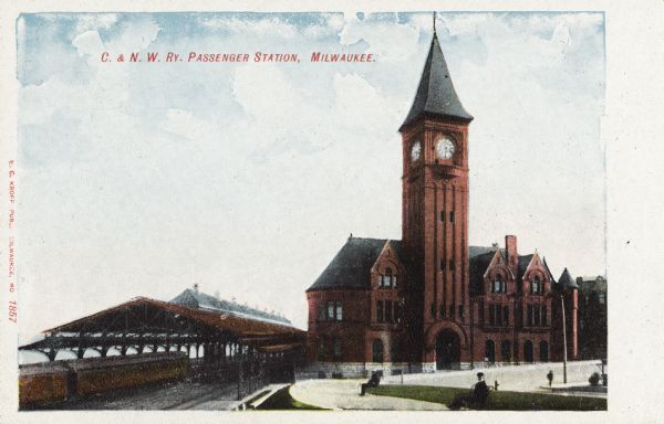 Chicago & Northwestern Railway Passenger Station, which was at the end of Wisconsin Avenue.  The station has a clock tower and an arched entrance. On the bottom left are two train cars partially under the train shed which has skylights, which covers the railroad tracks next to the platform. Men sit on benches in front of the station. Caption reads: "C. & N. W. Ry. Passenger Station, Milwaukee."