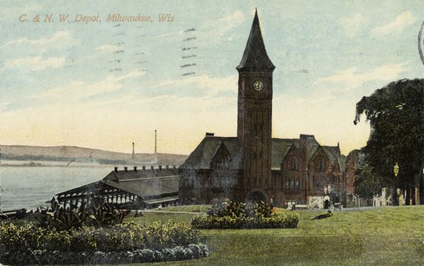 Chicago & Northwestern Railway Depot, with train shed and clock tower.  In the foreground is a landscaped area with flowers. In the background is Lake Michigan. Caption reads: "C. & N. W. Depot, Milwaukee, Wis."