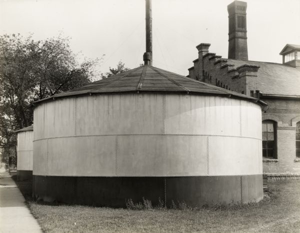 Storage Tank #2. A large, rounded tank with a conical roof.  Another tank is directly behind.  A large brick building is on the right.