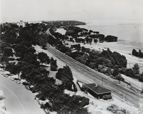 Aerial view looking north from the foot of Milwaukee's main thoroughfare, Wisconsin Avenue. Lincoln Memorial Drive winds its way along the lagoon in Juneau Park. In the background is the Milwaukee Yacht club, located on the harbor, with Lake Michigan in the upper right. Railroad tracks and trees separate the two roads.