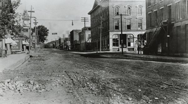 Looking east down dirt road. Commercial buildings and storefronts line the road.