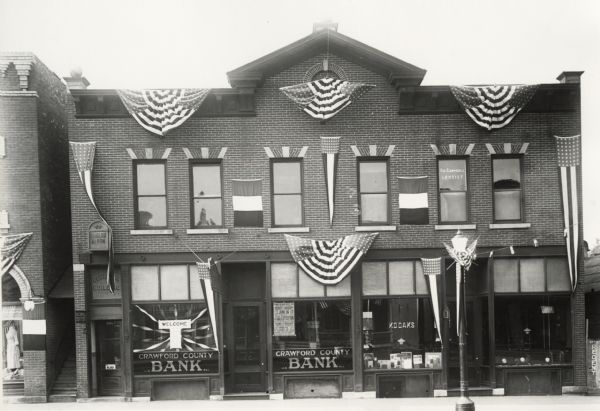 Decorated for the 250th celebration of the discovery of the Mississippi River. The ribbons and banners are all American flag themed. The storefront to the right of the bank is advertising Kodaks.