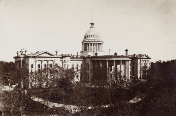 Elevated view of Wisconsin's Third Capitol building. A path in front of the building can be seen through the trees that surround the grounds.