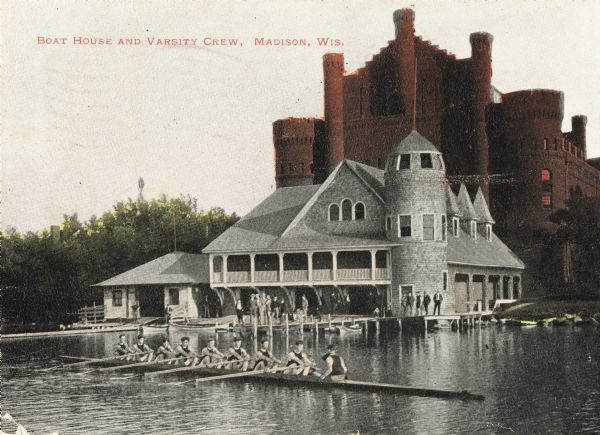 View towards shoreline from Lake Mendota of University of Wisconsin-Madison varsity men's rowing crew. People are watching from the boathouse in the background. Behind the boathouse is the Armory (Red Gym or Old Red). Caption reads: "Boat House and Varsity Crew, Madison, Wis."
