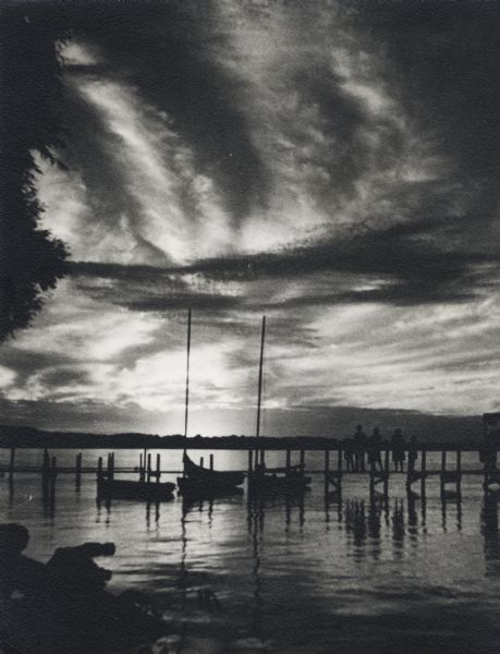 The sun is setting in the distance with three small boats docked at the pier.