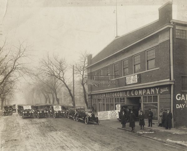 Garage and automobile lot which appears to be at 16-20 East Doty Street. Men stand on the sidewalk in front of the building, and signs advertise the recent arrival of <i>35 Car Loads of Buicks</i>. A large group of the Buicks are parked in the street.