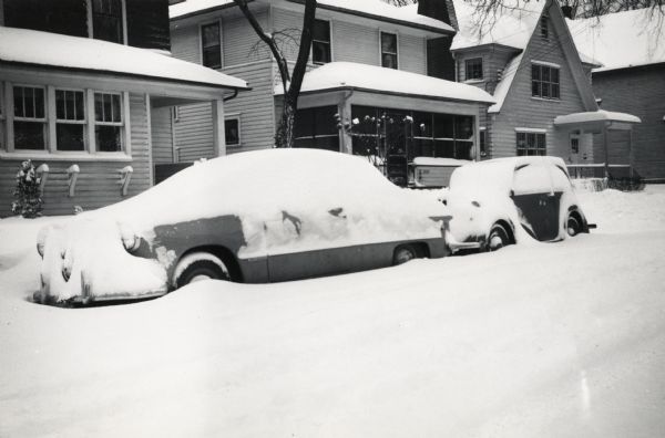 View from street of house numbers 2813-2817 Center Avenue. Two cars parked on the road are covered in snow.