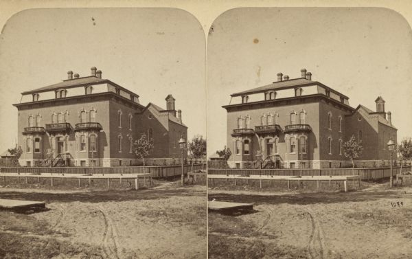 Stereograph. The house stands back from a dirt road behind a fence and yard.