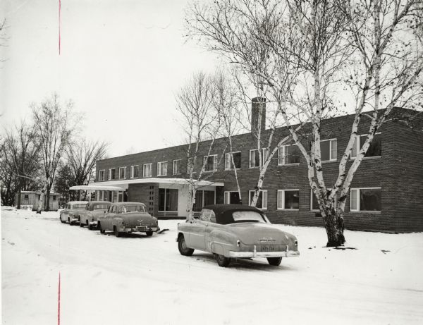 Exterior of hospital in winter, with four cars parked in front.