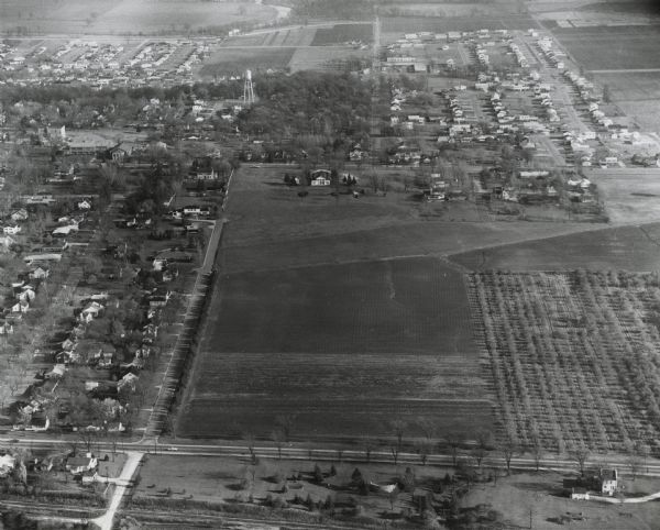 Aerial view includes farm and orchards, surrounded by neighborhoods. A water tower is on the upper left half.