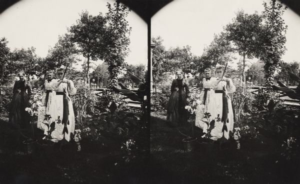 Stereograph. The woman in front is displaying a Muskellunge, caught in Long Lake, on the residential lawn of M. Newman. Two other woman are standing behind her. Another house is on the right.