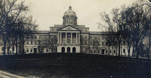 Exterior view of front of Main Hall (now Bascom Hall) on University of Wisconsin-Madison campus.  A person with a tripod is on the hill in front of the hall.