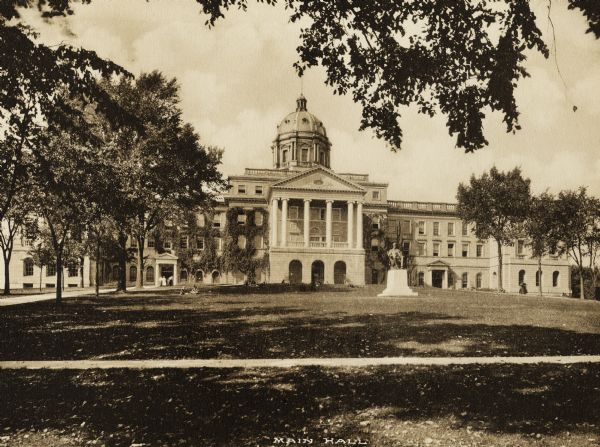 Bascom Hall with dome (formerly Main Hall) from Bascom Hill on the University of Wisconsin-Madison campus. The Lincoln Monument is in front of the entrance. Pedestrians are on the lawn and near a side doorway.