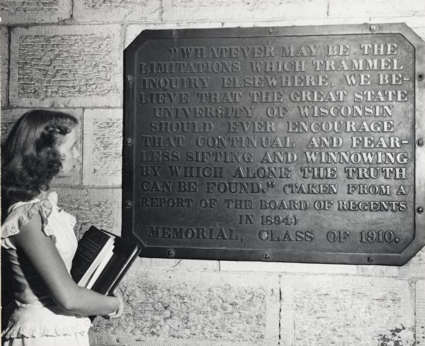Girl standing next to "Sifting and Winnowing" memorial plaque at the entrance to Bascom Hall (formerly Main Hall) on the University of Wisconsin-Madison campus. The memorial was donated by the Class of 1910.