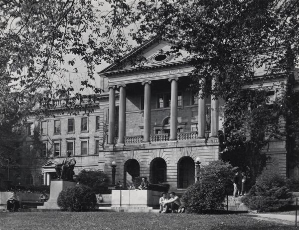 Exterior of entrance to Bascom Hall (formerly Main Hall) on the University of Wisconsin-Madison camppus. Students are sitting around the Lincoln Monument on Bascom Hill.