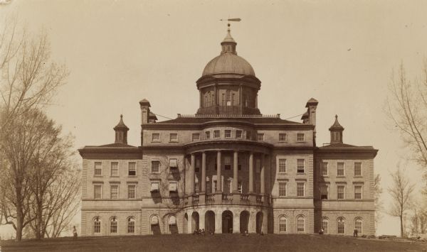 Exterior of Bascom Hall with dome (formerly Main Hall) on the University of Wisconsin-Madison campus. People are sitting and walking on the lawn.  For a rear view of Bascom Hall see ID 58147.